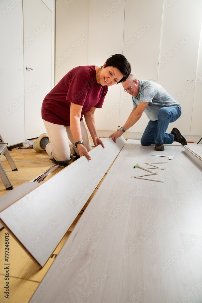 Senior couple installing laminate flooring in their new home together. DIY concept. Mature woman and man are doing renovation. Senior couple installing laminate flooring in their new home together. DIY concept. Mature woman and man are doing renovation.