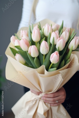 A large bouquet of tulips wrapped into white paper, holded by a young woman