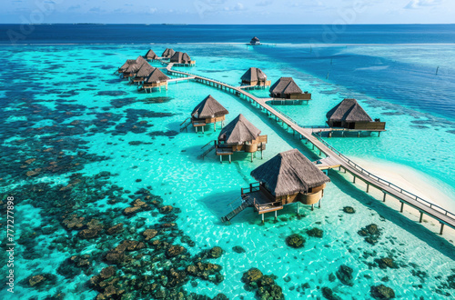 An aerial view of an island in the Maldives with overwater bainment and cabanas, and clear blue waters around it, a dock leads to one main house on top of sand bar photo