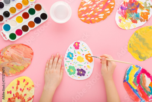 Photography Baby girl holding paintbrush and painting colorful egg on paper with watercolor on pastel pink table background