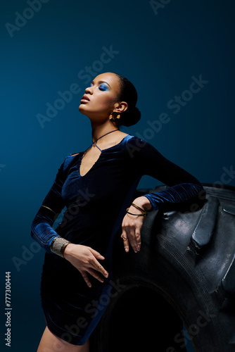Schilderij op canvas A young African American woman stands beside a towering black bag in a studio setting