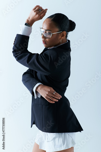 Young African American woman dressed in a suit and glasses, striking a pose in studio