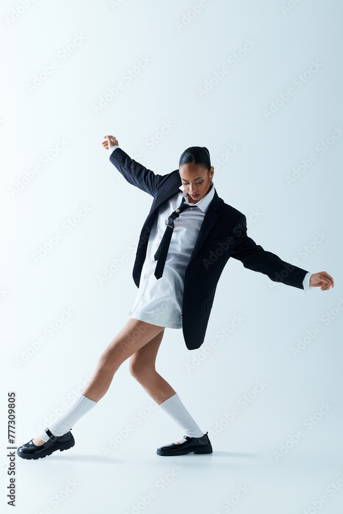 A young black woman in a stylish suit and tie joyfully dancing in a studio.