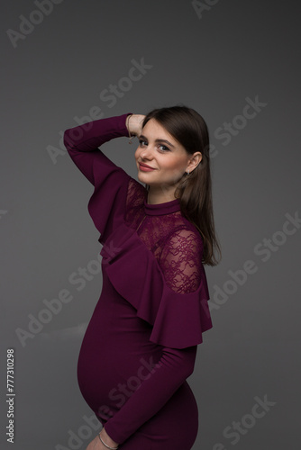 portrait of a pregnant woman in a purple dress on a grey background