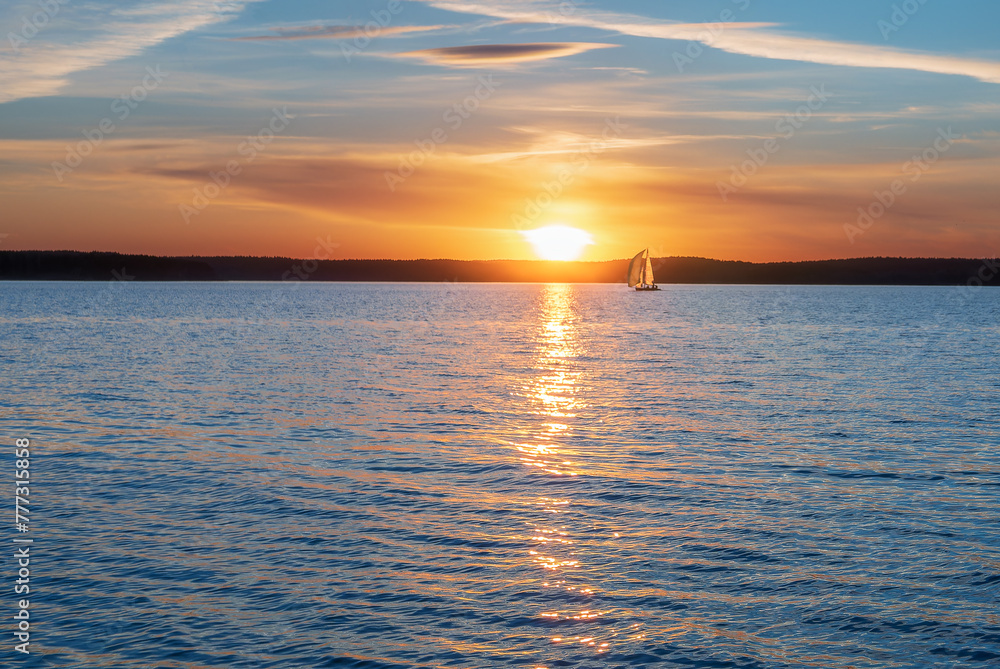 A sailing yacht against the background of the setting sun. Calming water evening landscape