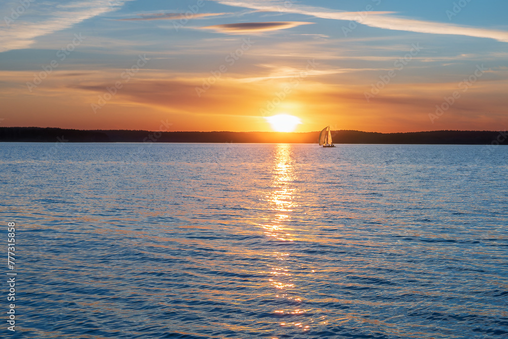 Obraz premium A sailing yacht against the background of the setting sun. Calming water evening landscape