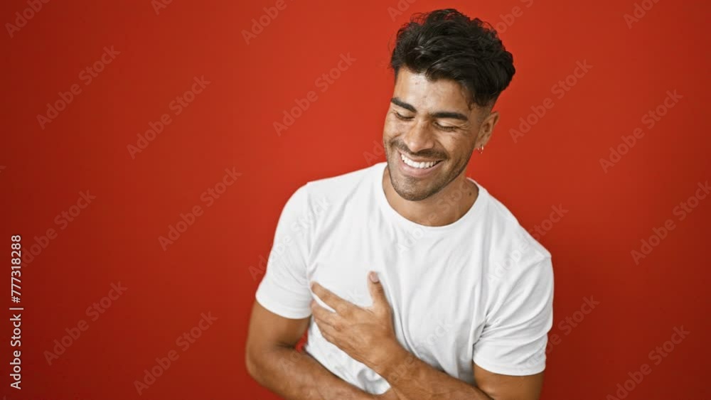 A young hispanic man with a beard smiles and points at the camera against an isolated red background A young hispanic man with a beard smiles and points at the camera against an isolated red background