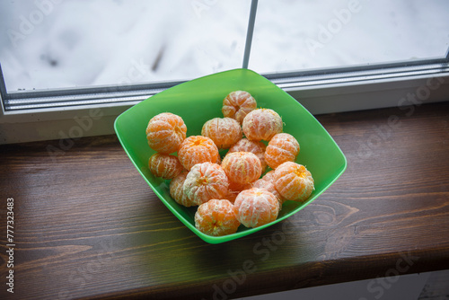 A bowl of peeled oranges sits on a wooden table. The peeled oranges are ripe and ready to eat. The scene is cozy and inviting, with the oranges adding a pop of color to the room