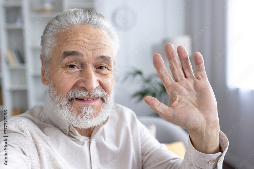 Smiling senior man waving hello in a bright room Smiling senior man waving hello in a bright room