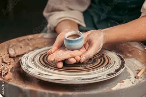 A person is holding a ceramic cup in their hands while working on a pottery wheel. Concept of creativity and craftsmanship, as the person is focused on shaping the clay into a functional