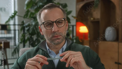 middle aged male psychologist in glasses sits in office, looking attentively and thoughtful. grey haired serious man in blue shirt working as therapist on season, holds pen and notebook, listening