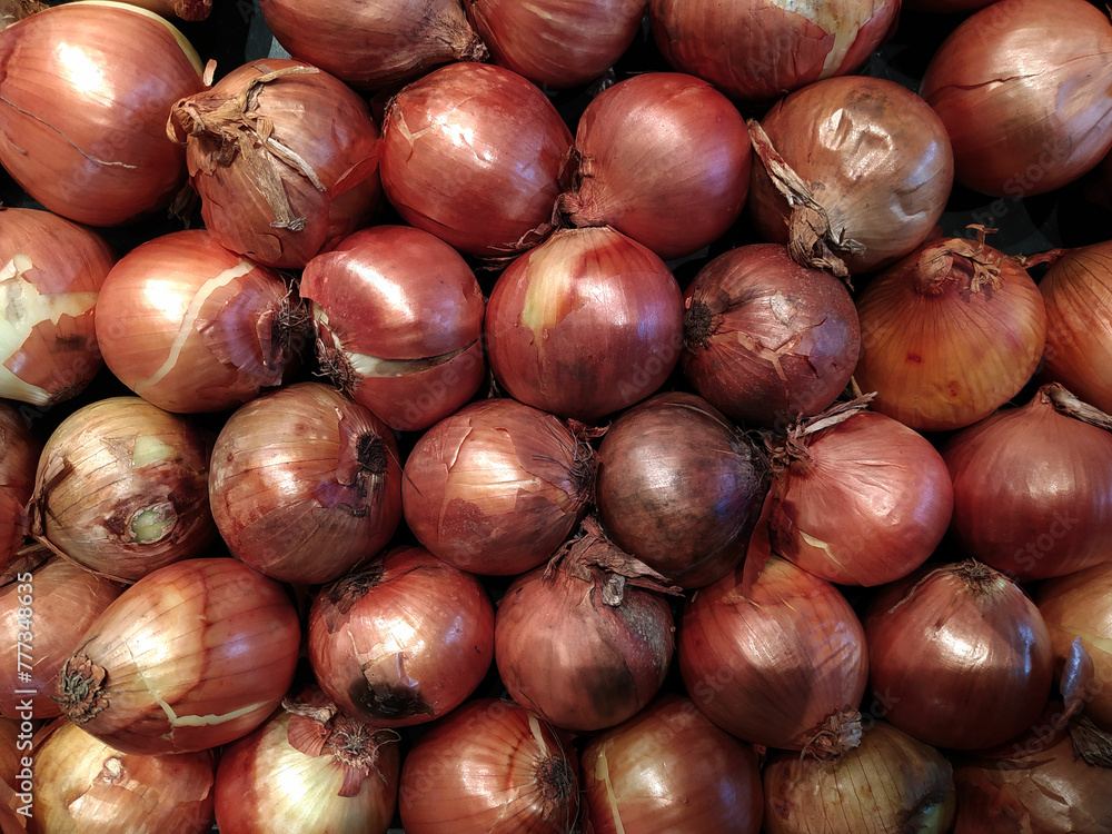Obraz premium Fresh onions on the table in the store, close-up. Vitamin seasoning for a healthy diet. A spicy food ingredient. A slide, a bunch of onions. Market tent, retail and wholesale. Trading place, market. A