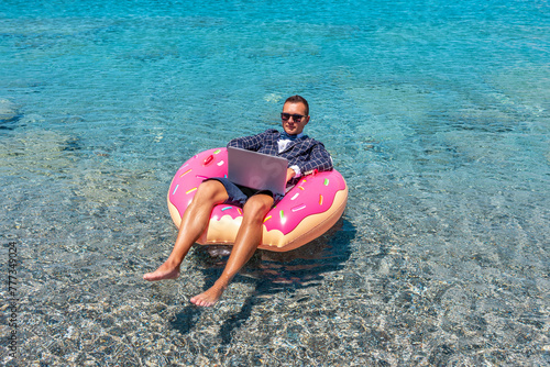 Businessman using laptop computer on an inflatable donut in the sea.