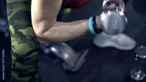 Middle-aged strong and independent woman in sportswear pumping hands muscles close-up with dumbbells in gym. Workout of athlete train inside fitness hall. Age fitness or training. Healthy lifestyle. photo