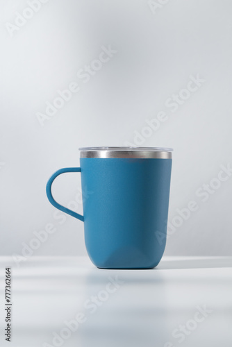 Blue tumbler made of stainless steel on a wooden table and white background.