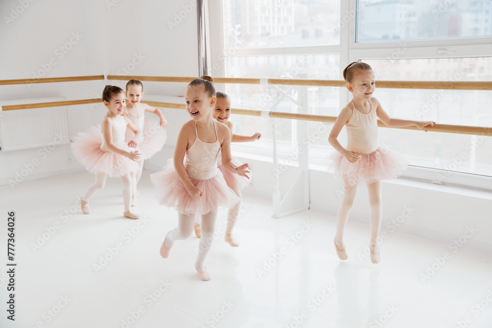 Naklejka premium Child ballerinas, little girls in mid-dance, capturing dynamics of ballet lesson. Classical ballet school. Concept of art, sport, education, hobby, active lifestyle, leisure time.