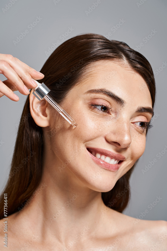 happy young woman with brunette hair smiles as she applying serum with cosmetic pipette in a studio setting. happy young woman with brunette hair smiles as she applying serum with cosmetic pipette in a studio setting.