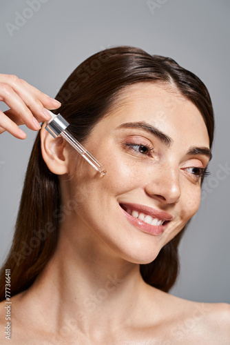 happy young woman with brunette hair smiles as she applying serum with cosmetic pipette in a studio setting.