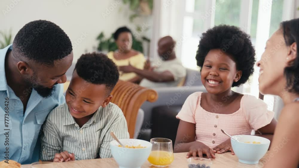 Family indoors at home at kitchen counter eating breakfast with grandparents in background - shot in slow motion Family indoors at home at kitchen counter eating breakfast with grandparents in background - shot in slow motion