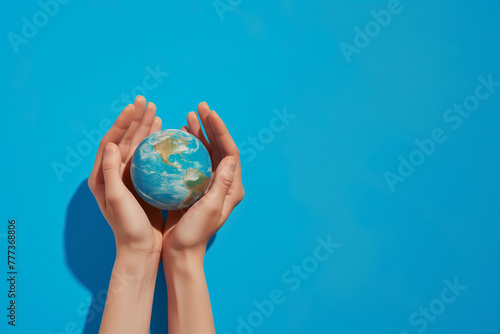 Terre ou mappemonde tenue par 2 mains humaines pour la protéger. Concept : Journée de protection de la Terre, 22 avril, prendre soin de la planète Terre. Fond bleu avec espace négatif Copy space  photo