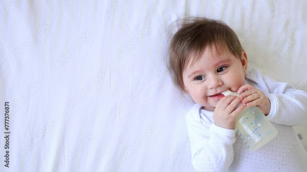Baby newborn girl sucks a bottle of milk lying on her back in a crib in white clothes, baby food concept, close-up Baby newborn girl sucks a bottle of milk lying on her back in a crib in white clothes, baby food concept, close-up