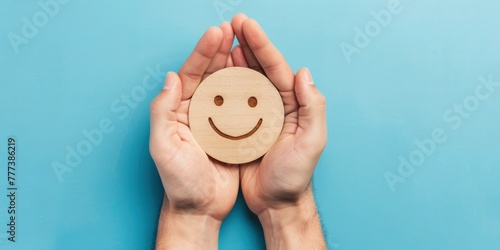 A man hands hold a wooden smiley face icon on a blue background with copy space, in a top view. happy, positive mood concept.