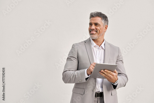 Happy mature business man using digital tablet isolated on white background. Middle aged ceo executive wearing suit, older businessman professional entrepreneur looking away at copy space.