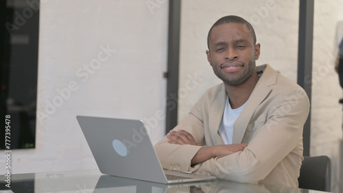 African American Man Smiling at Camera while Working on Laptop in Office