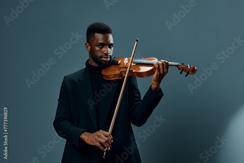 Elegant African American man in black suit playing violin on vibrant blue background with passion and skill