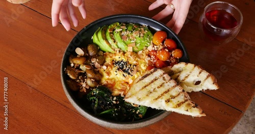 Woman waiter puts plate with large and nutritious breakfast on table. A juicy looking and beautiful dish served at popular restaurant in Bali. Close view of food, only hands of woman in frame