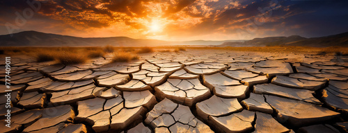 Sun sets over a cracked earth desert landscape. Severe drought and climate change effects. World Soil Day. Panorama with copy space.