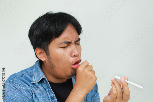 Murais de parede Smoker holding a cigarette suffering from chronic cough, Asian man patient coughing with respiratory problems, emphysema disease or lung cancer from smoking, medical and health care concept