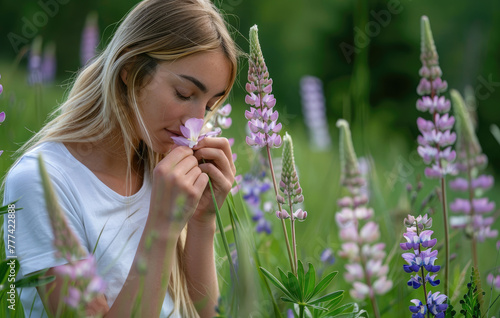 Young woman in white tshirt standing near purple flowers of pinklupine  holding flower and smelling it  spring meadow with tall grasses