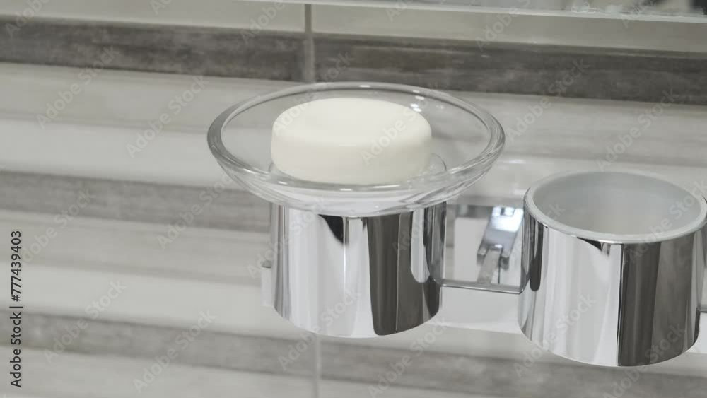 man's hand puts piece of round soap in glass soap dish, selective focus, slow motion
