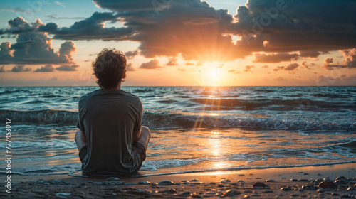 Young man meditating on the beach at sunset. Rear view. photo