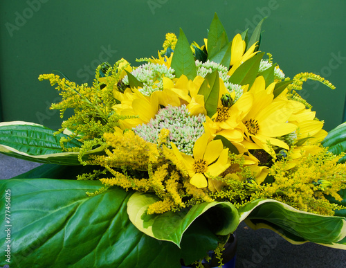 Close-up of fresh bouquet with flowers and leaves in yellow and green from the garden in summer against green background.