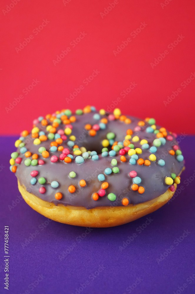 Donut with lilac glaze and sprinkles on pink and purple background Donut with lilac glaze and sprinkles on pink and purple background