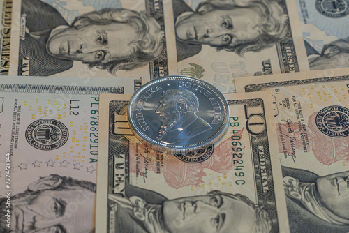 Silver coin, Krugerrand with US Dolars (USD)  notes in background.  © PIOTR