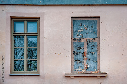Architectural detail of a window and painted fake window next to it. Peeling paint on the wall.