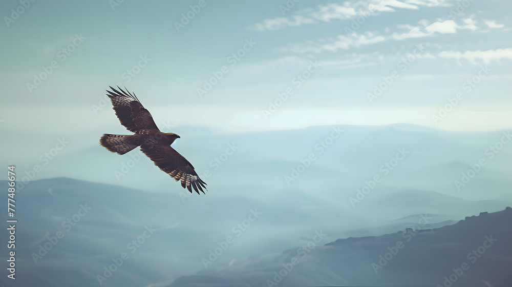 Fototapeta premium A solitary hawk soaring gracefully through a vast, blue sky, with distant mountains fading into a hazy, blurred horizon