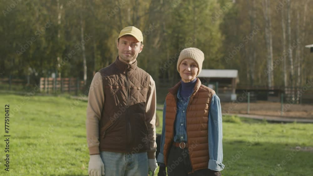 Medium slowmo portrait of happy Caucasian couple of farmers standing on green sunny pasture and posing for camera Medium slowmo portrait of happy Caucasian couple of farmers standing on green sunny pasture and posing for camera