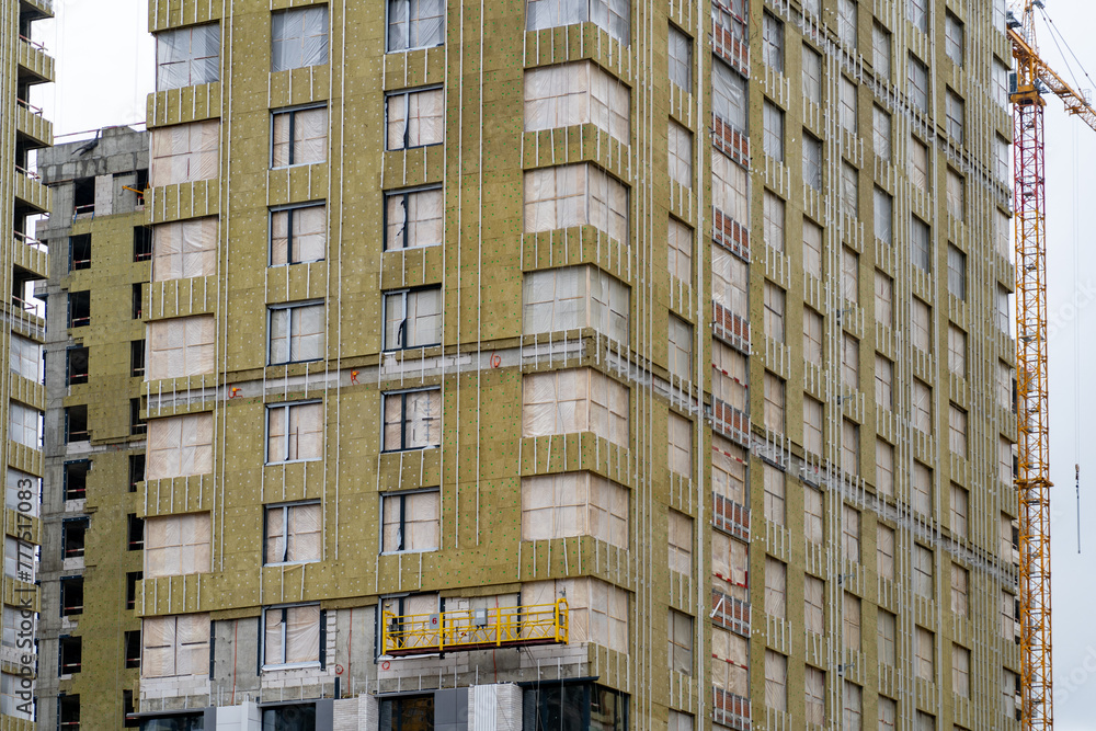 High-rise under construction with yellow insulation and exposed framework, next to a crane