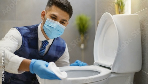 Young chambermaid with medical mask cleaning toilet bowl in bathroom photo