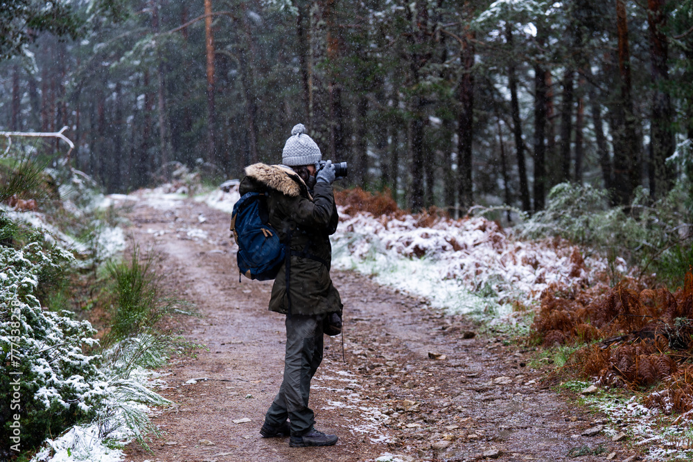 Profile portrait, brunette girl in green coat and gray hat photographs snowy woodland.