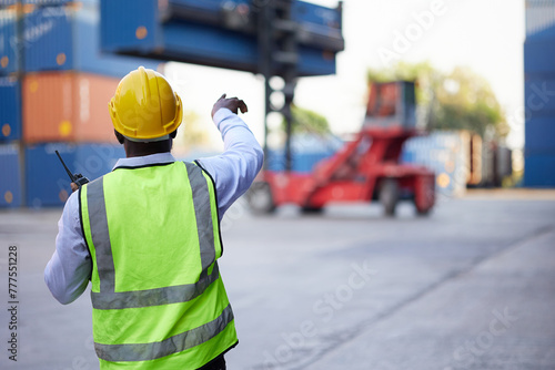 back view African worker or engineer using walkie talkie and showing gesture to crane car in containers warehouse storage