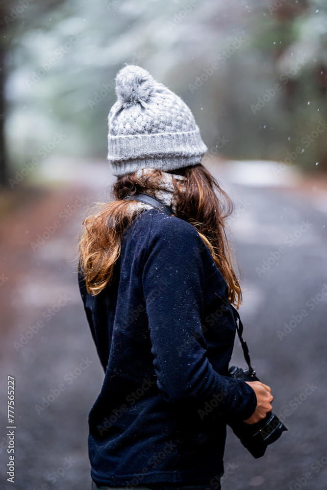 Unrecognizable brunette girl in gray hat and black fleece, trekking snowy forest trail.
