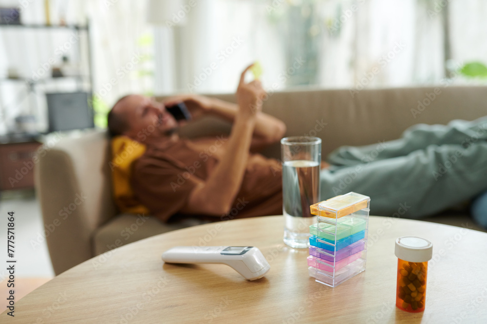 Pills and contactless thermometer on table of sick man calling doctor Pills and contactless thermometer on table of sick man calling doctor