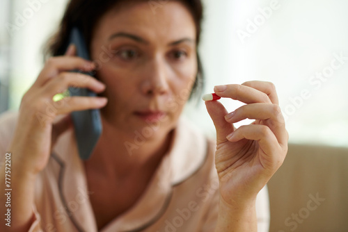 Sick woman looking at pill when calling doctor