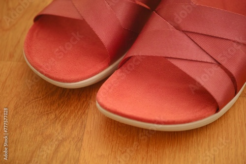 A close-up shot of a pair of red sandals on a wooden floor.