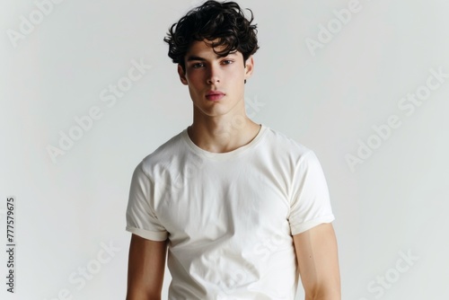 A young man in a white t-shirt poses with a natural, confident stance against a neutral background, ideal for fashion and lifestyle Mockups